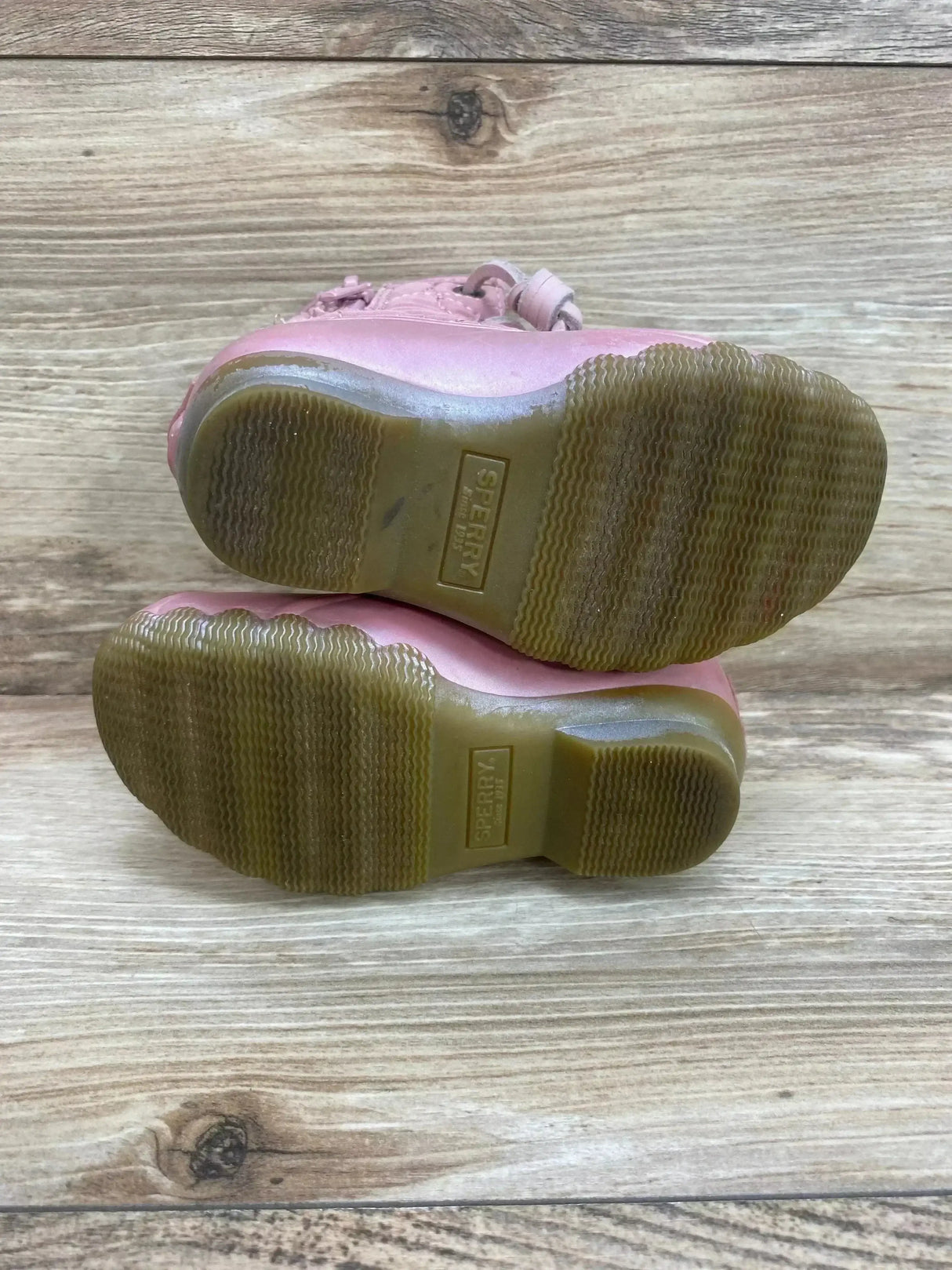 Bottom view of pink Sperry Saltwater duck boots showing rubber soles with light wear on wooden background