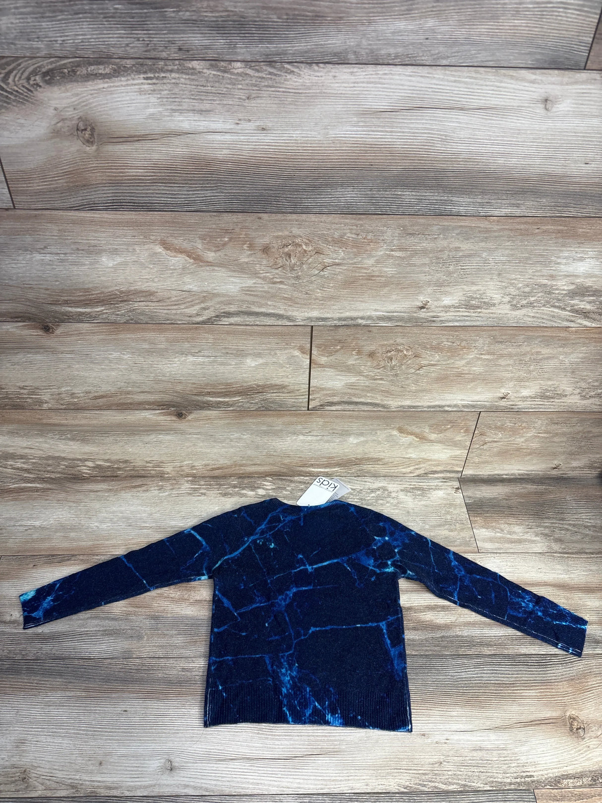 Dark blue kids sweater with turquoise abstract pattern laid flat on wooden floor