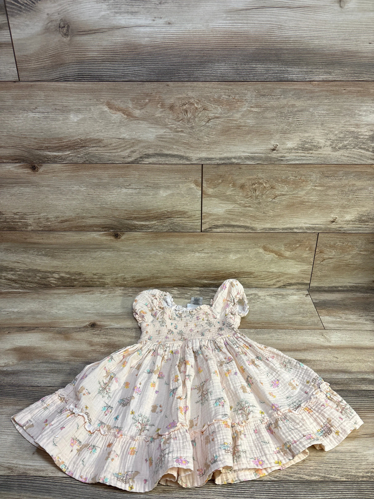 Flat lay of Bonnie Jean smocked gauze dress in beige, smocked bodice, flutter sleeves, ruffled hem on wood backdrop