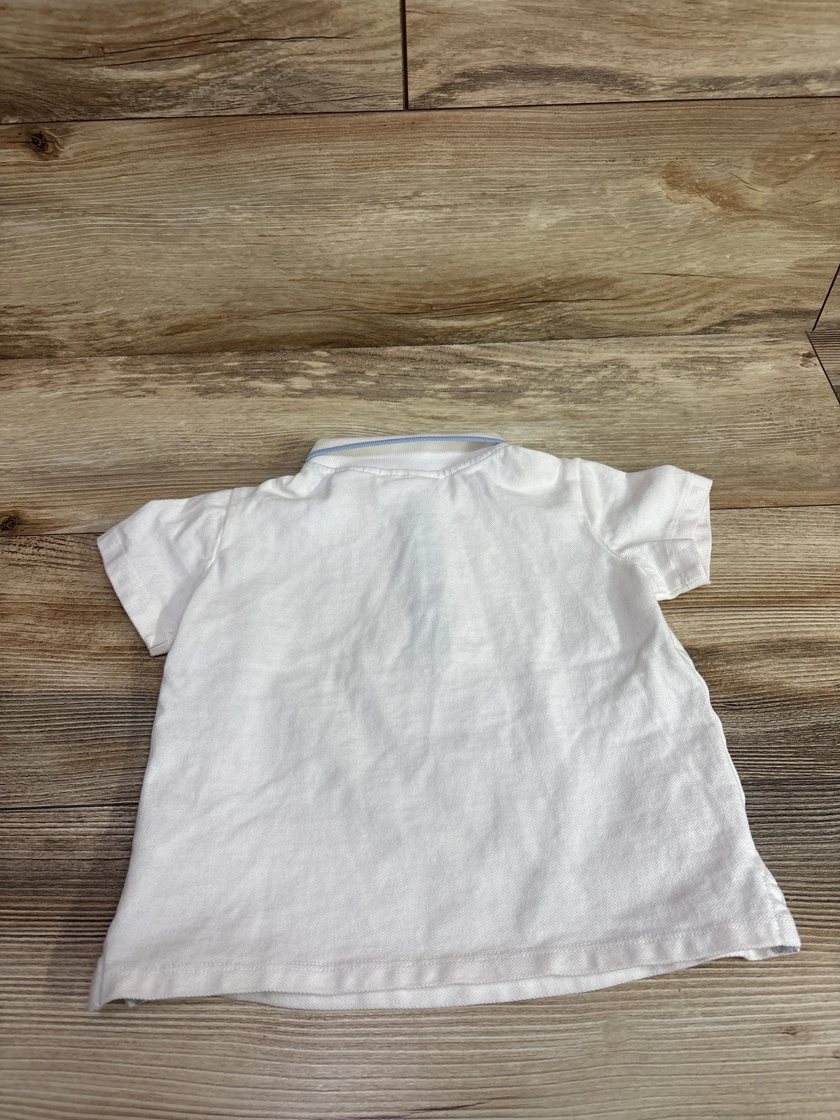 Back view of a white Tommy Bahama polo shirt for toddlers, size 24m, on a wood background.