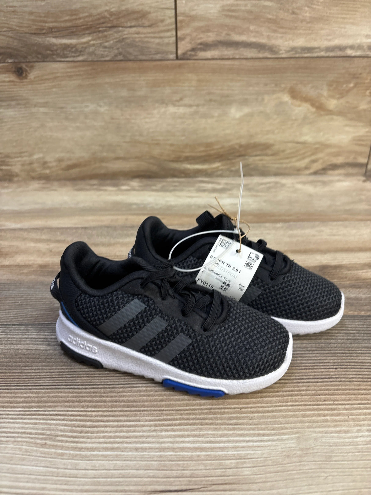 Side view of toddler black Adidas Racer TR 2.0 sneakers showcasing textured mesh upper and white cushioned sole on wooden floor, size 9C