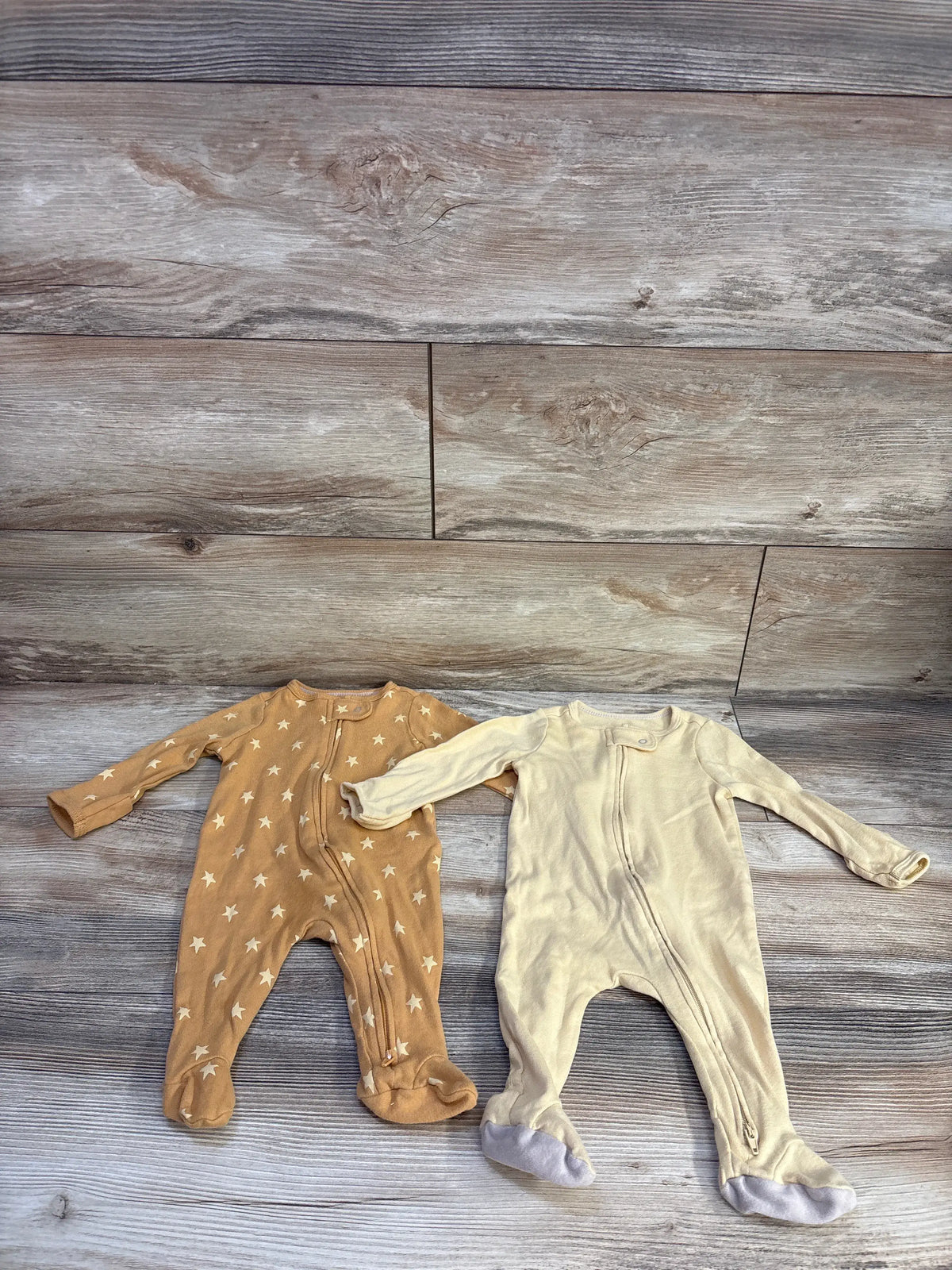 Front view of Cloud Island 2-pack sleepers in size 0-3 months showcasing star-print and solid yellow designs on a wood-look background