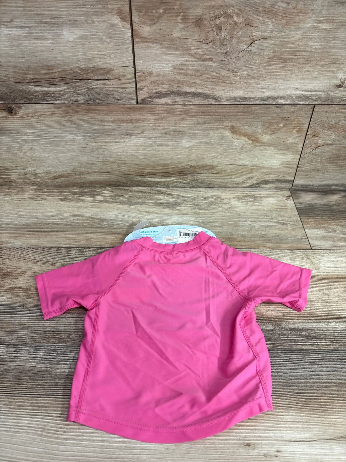 Back view of Green Sprouts toddler short-sleeve rashguard shirt showcasing hot pink color and raglan seams on wood floor background