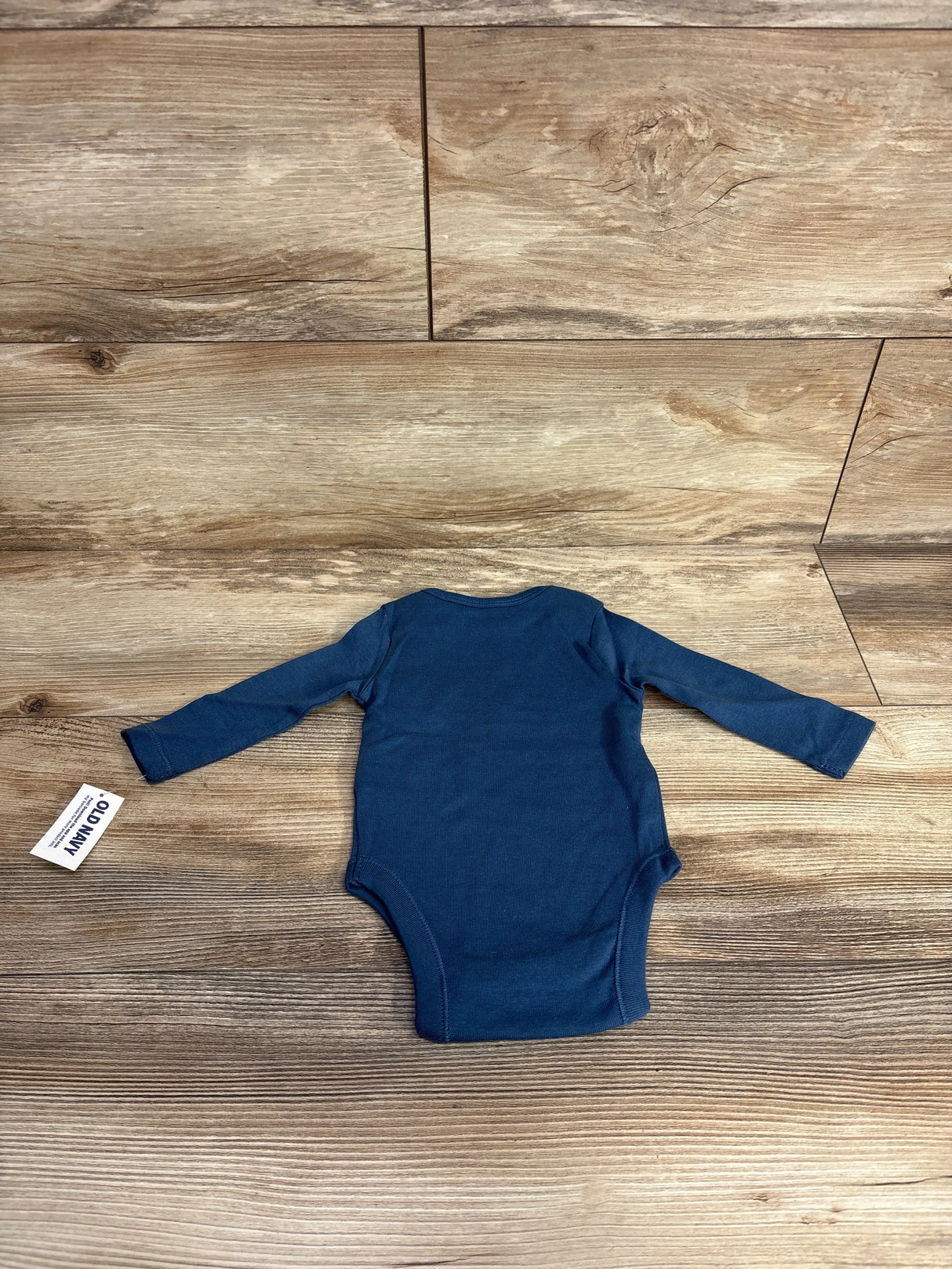 Back view of Old Navy blue long-sleeve baby bodysuit showcasing long sleeves and brand tag on wood background