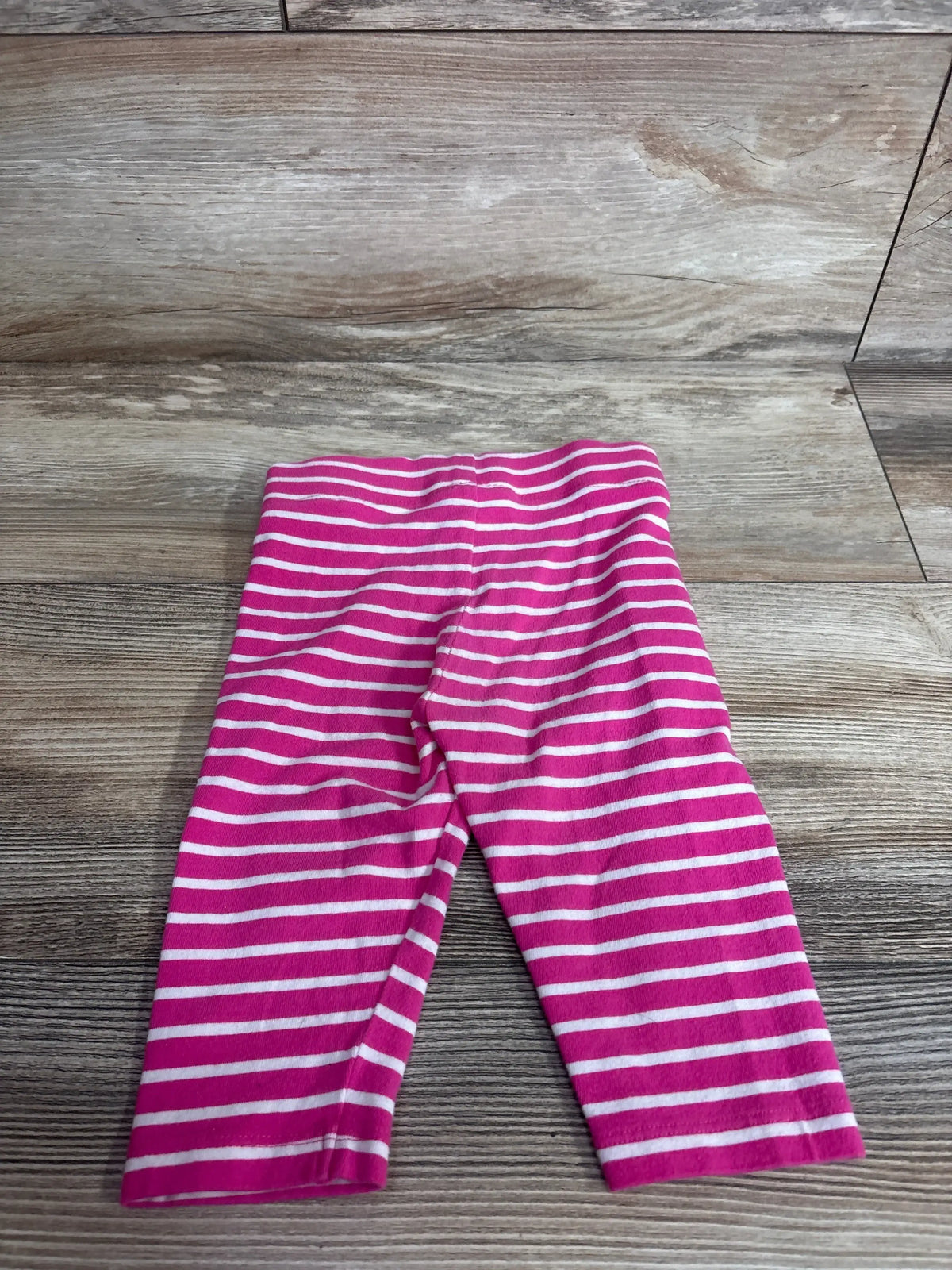 Flat lay of Mini Boden toddler leggings showcasing pink and white horizontal stripes and elastic waistband on wood plank background