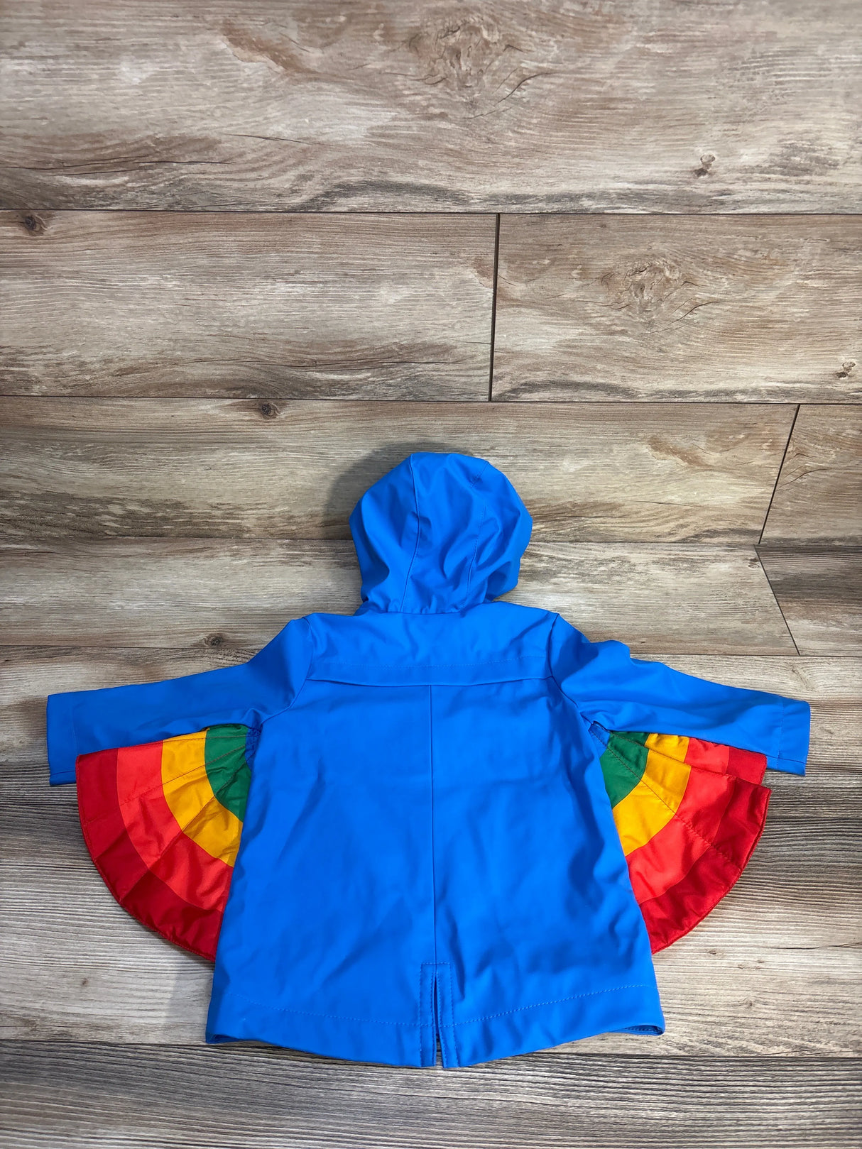 Back view of blue Cat and Jack toddler rain jacket (18 months) showing rainbow cape-like panels with wood floor background