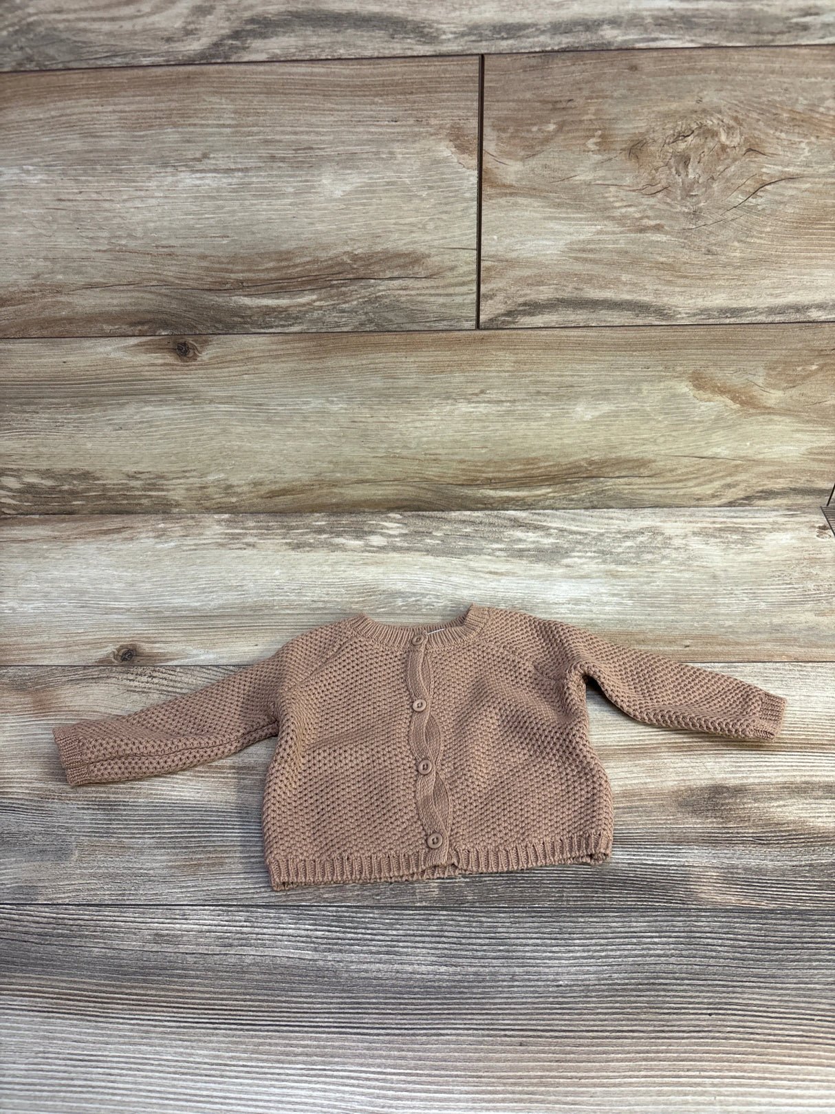 Flat lay of newborn brown organic knit baby cardigan showing front button closure and textured stitch on wood background
