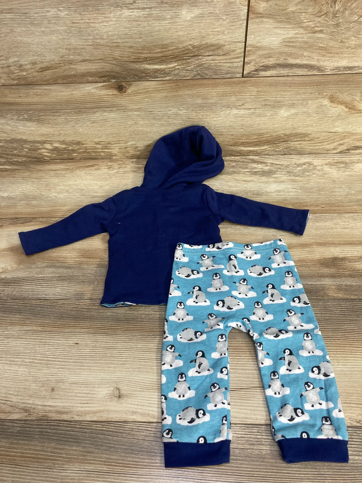 Flat lay of Harry and Violet reversible navy button-up top and matching penguin-print bottoms on wooden floor