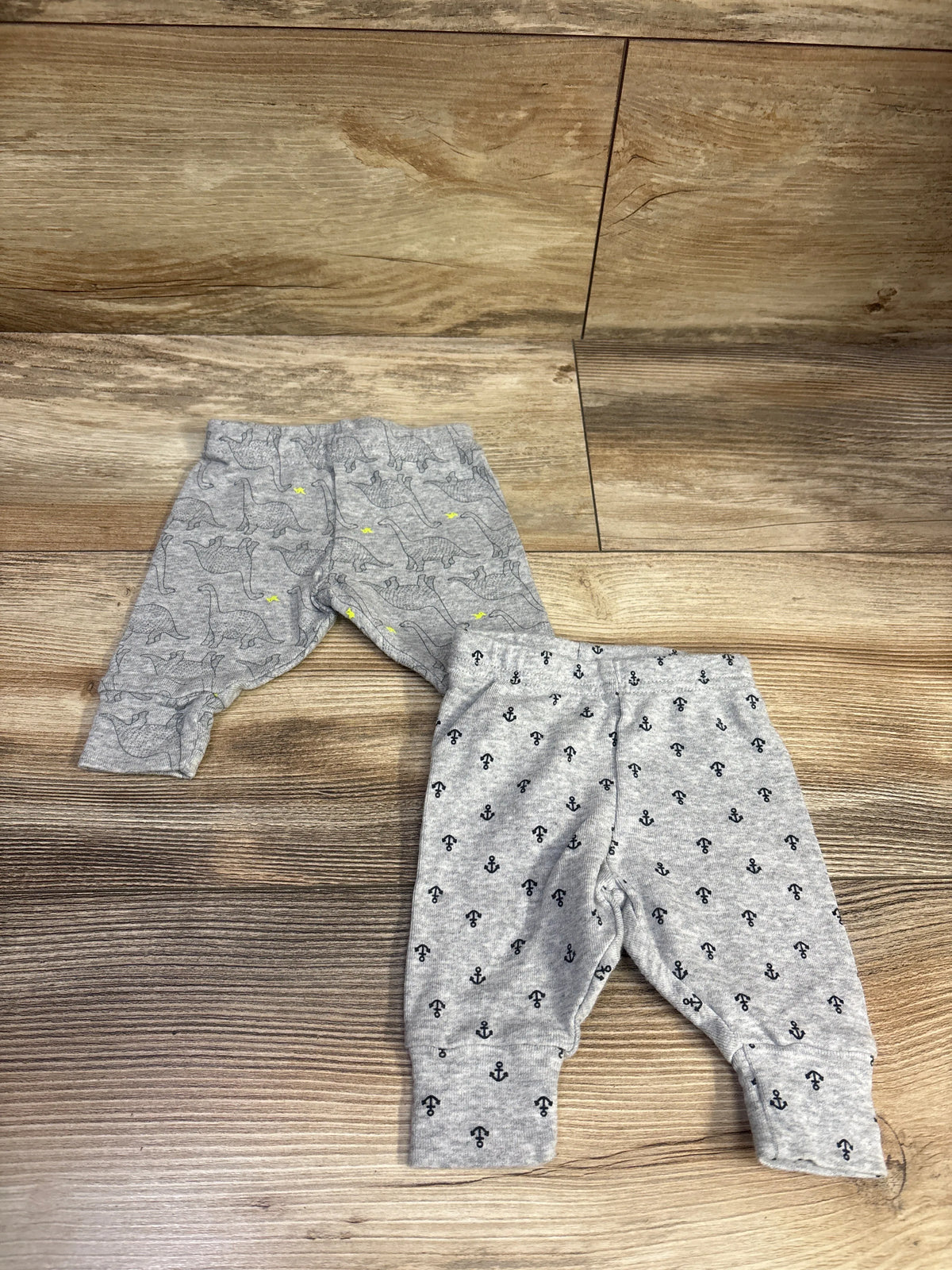 Top view of Simple Joys two-pack newborn pants showcasing dinosaur and anchor prints on a wood floor