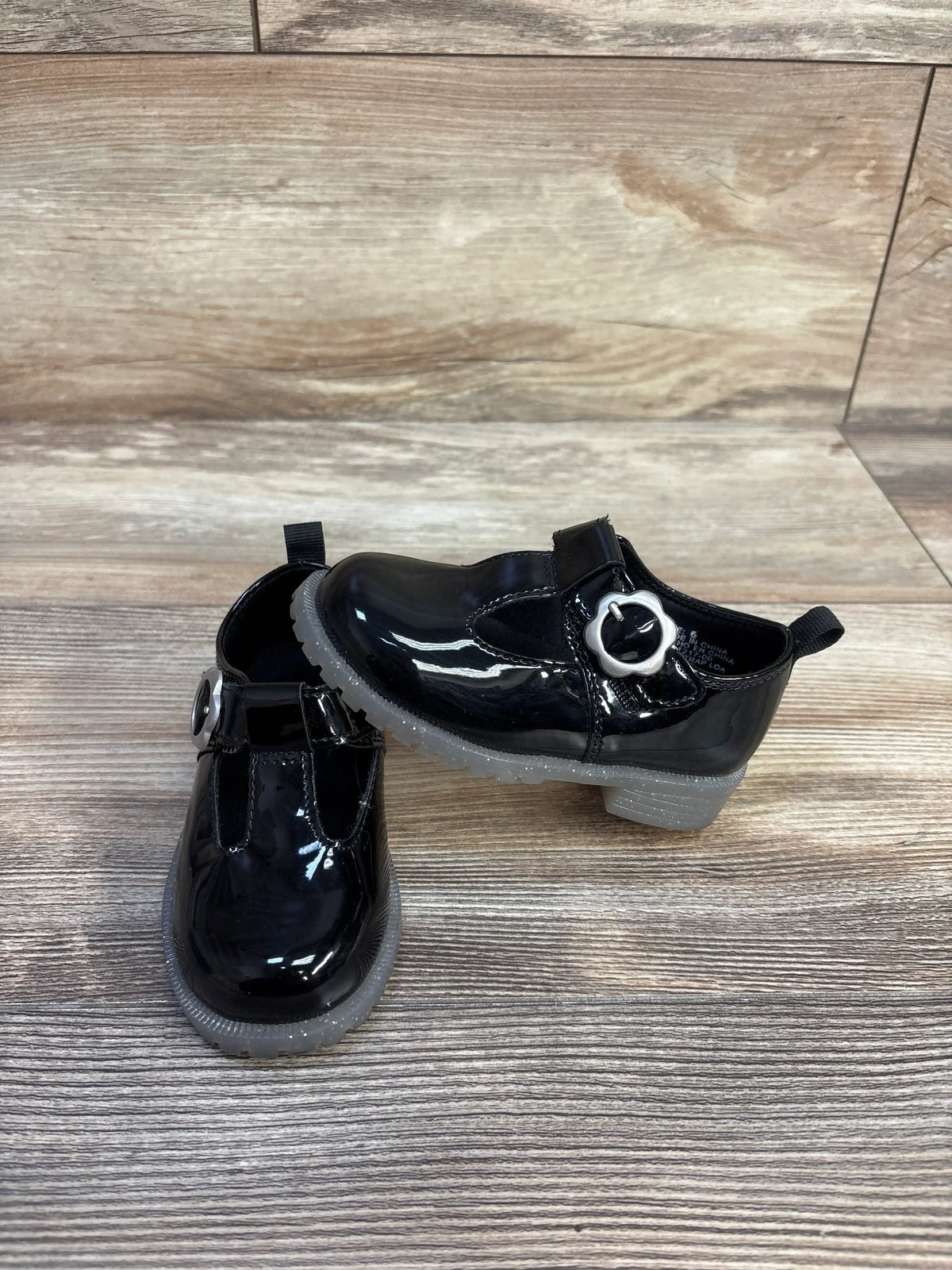 Angled view of Baby Gap T-strap loafers showcasing black vegan patent leather, metal buckle, and rubber gripper soles