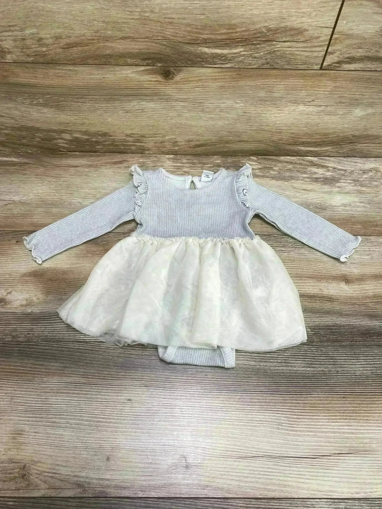 Flat lay of rib-knit metallic infant bodysuit dress with grey ruffled long sleeve top and ivory tulle skirt on wood floor