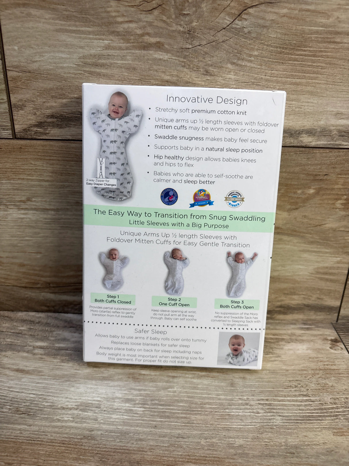 Back of Amazing Baby arms-up swaddle sack box showcasing feature text and three-step transition photos on wooden background