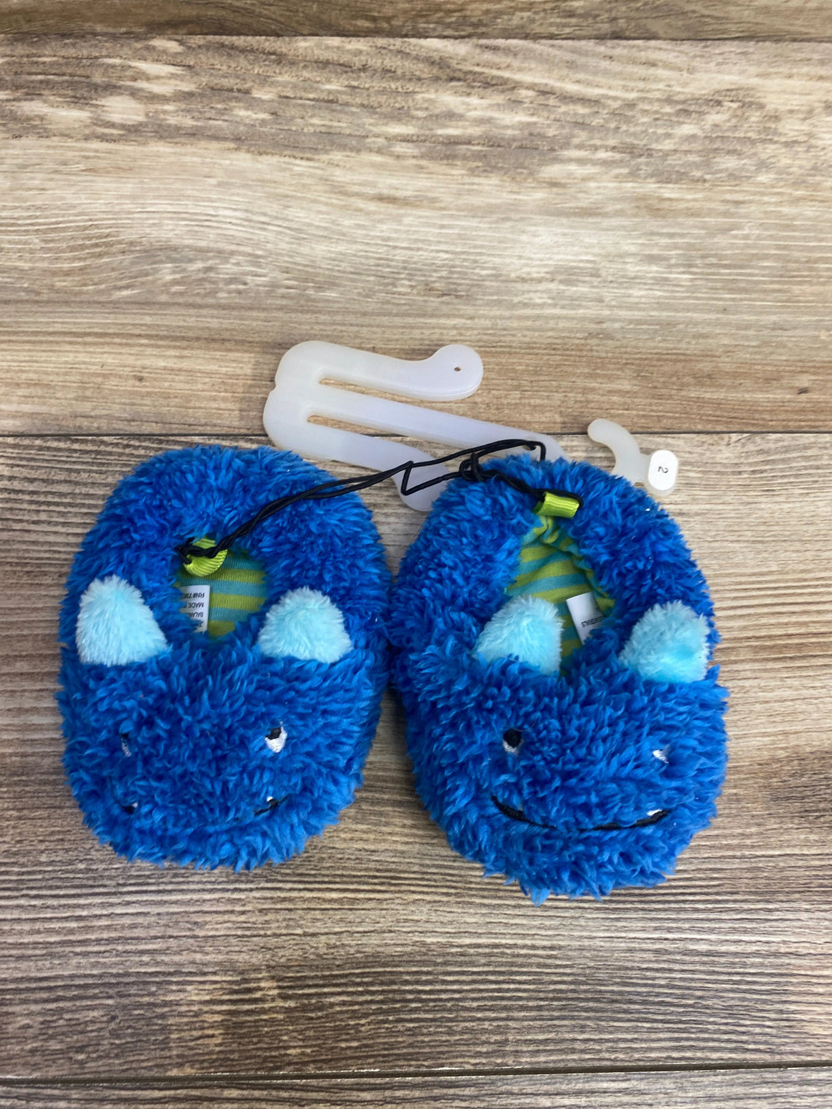 Blue fuzzy baby slippers with playful monster face and light blue ears on wooden background