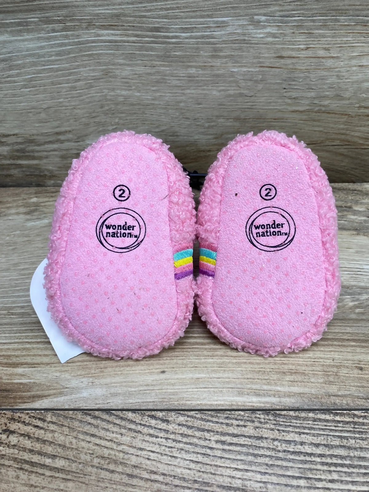 Top view of pink Wonder Nation bootie slippers showing rainbow side stripe and textured non-slip soles on wood background