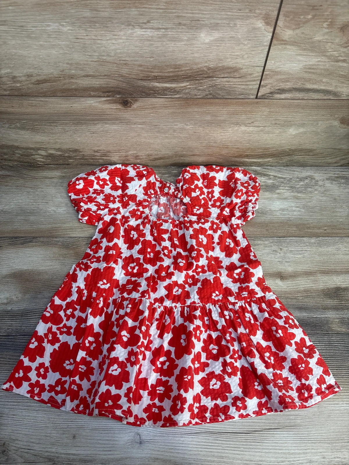 Red and white floral short sleeve baby dress with ruffle skirt on wood background