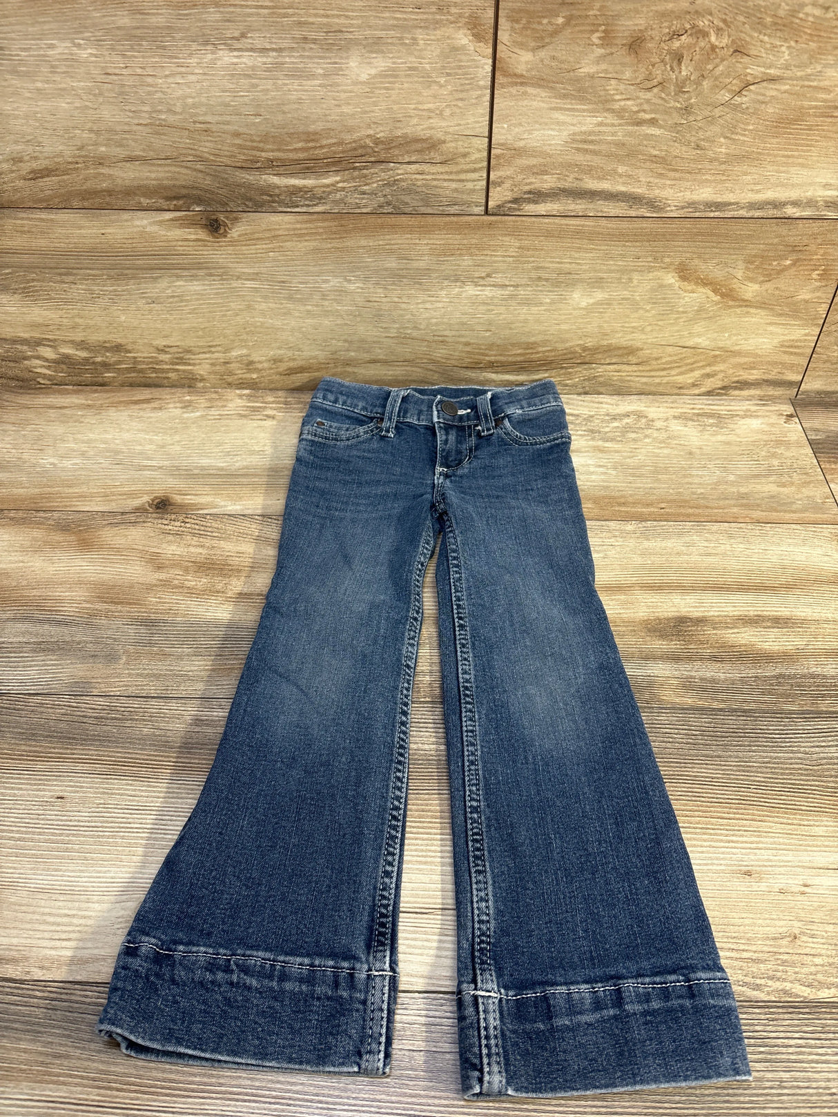 Front view of Wrangler toddler blue slim flared jeans size 4T showcasing flared legs and cuff detail with wood floor background