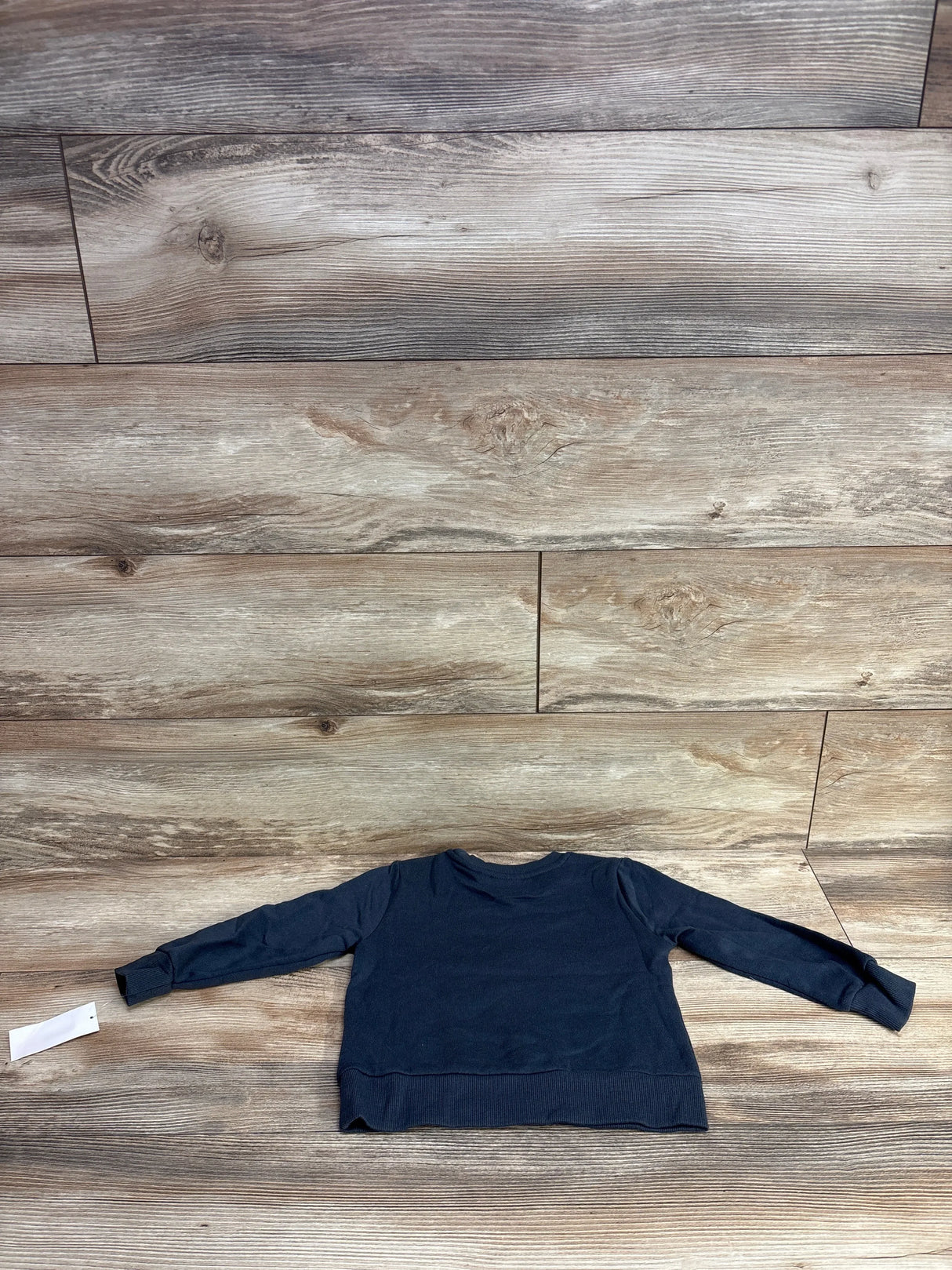 Flat lay of Marvel Black Panther sweatshirt in dark navy with long sleeves and attached hangtag on wood plank background
