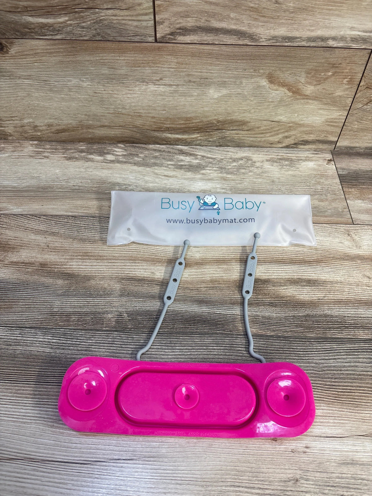 Top-down view of Busy Baby mini mat toy straps in pink showing two gray adjustable straps and three pink suction cups on a wood floor