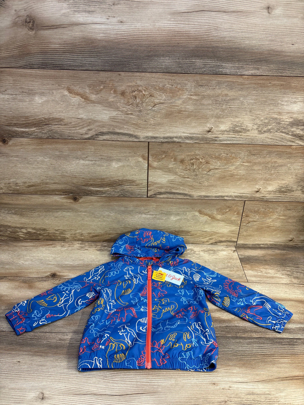 Front flat lay of Cat and Jack windbreaker jacket 2T with hood, red zipper and multicolor dinosaur on wood floor