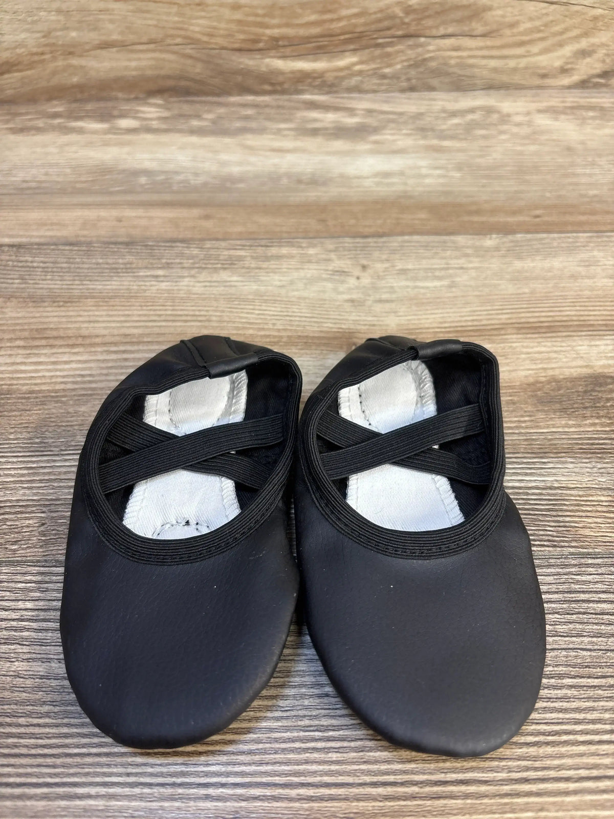 Black toddler ballet slippers with elastic straps on wood background