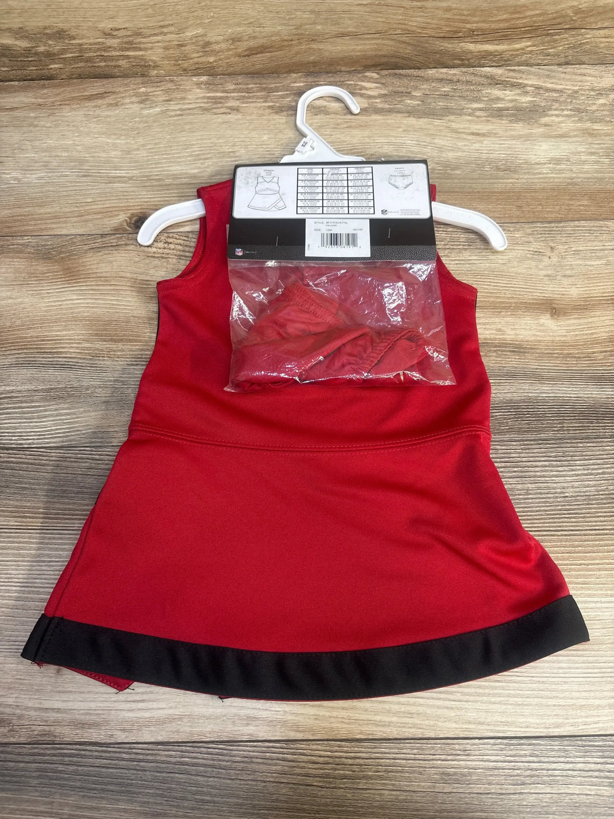 Flat-lay of toddler Atlanta Falcons cheer jumper dress showing sleeveless red body, black hem trim, and packaged matching underwear on wood background