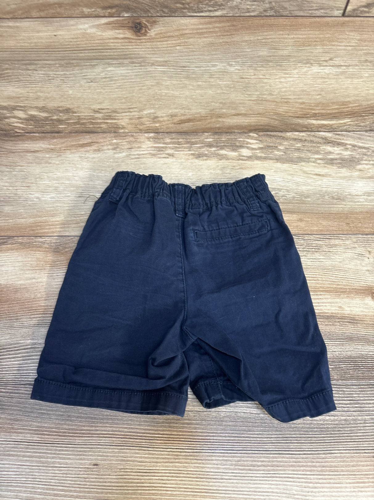 Navy blue kids shorts with elastic waist, laid flat on wood floor for resale