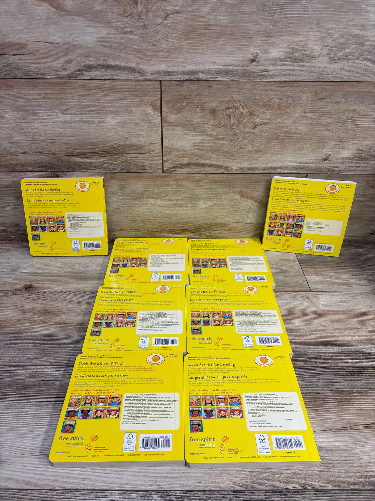 Overhead view of Lakeshore Best Behavior bilingual set of 8 board books showing yellow back covers and barcode labels on a wood background