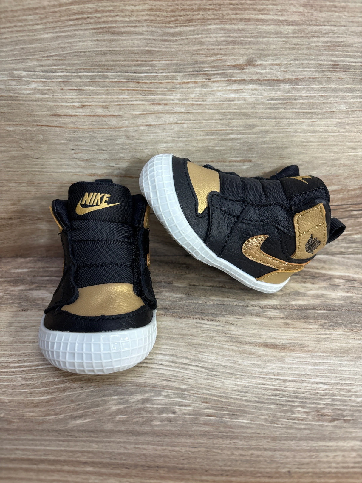 Pair of black and gold Nike baby shoes with white soles on wood surface, kids footwear