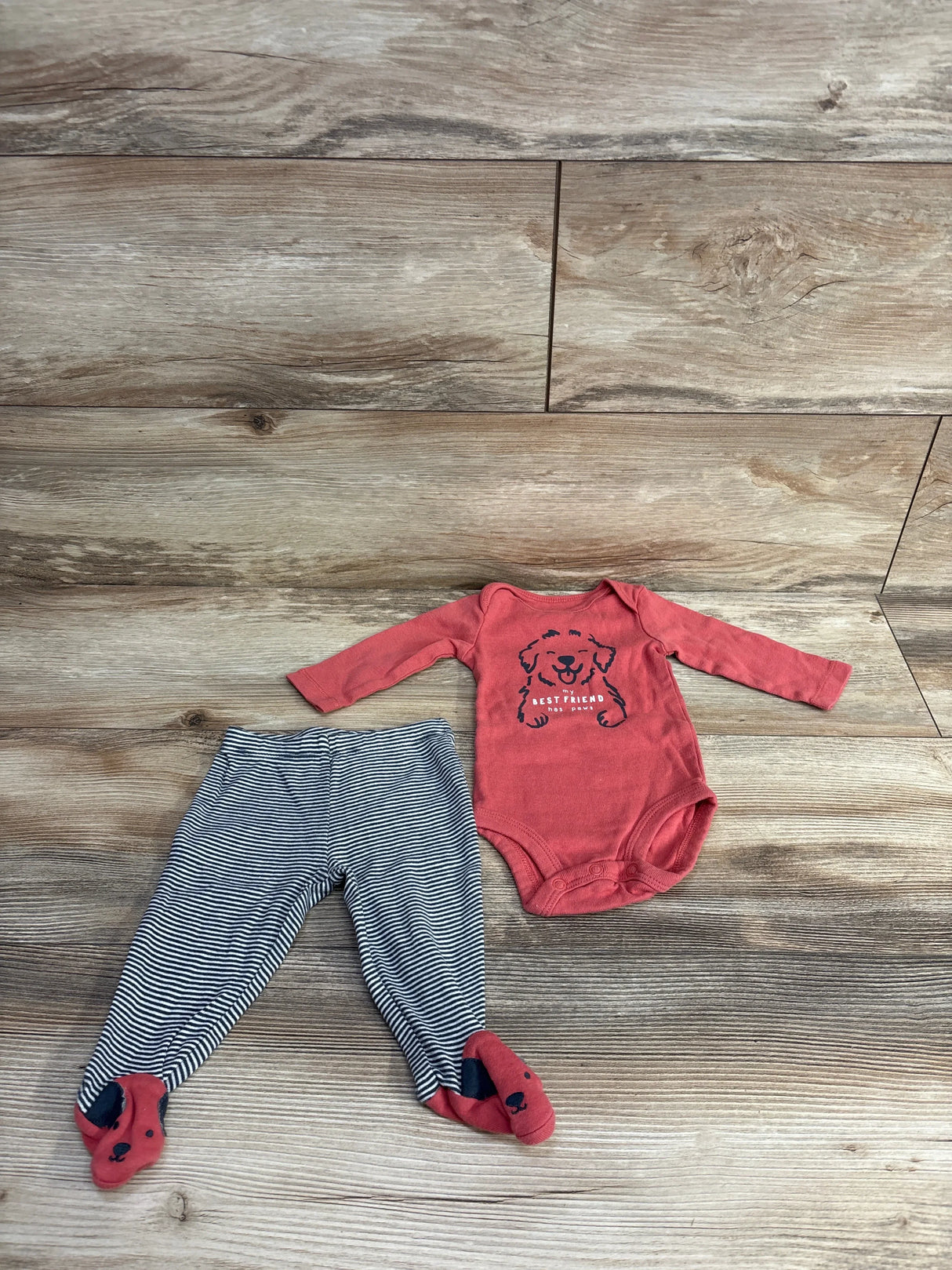 Flat lay of baby outfit showing red Best Friend dog print bodysuit and navy striped footed pants with dog feet on wood floor