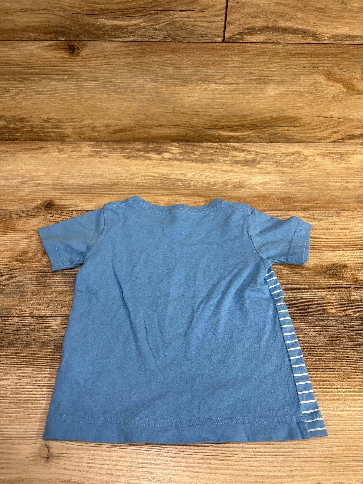 Back view of blue Hurley shirt in size 2T showcasing short sleeves and striped side panel on a wood surface