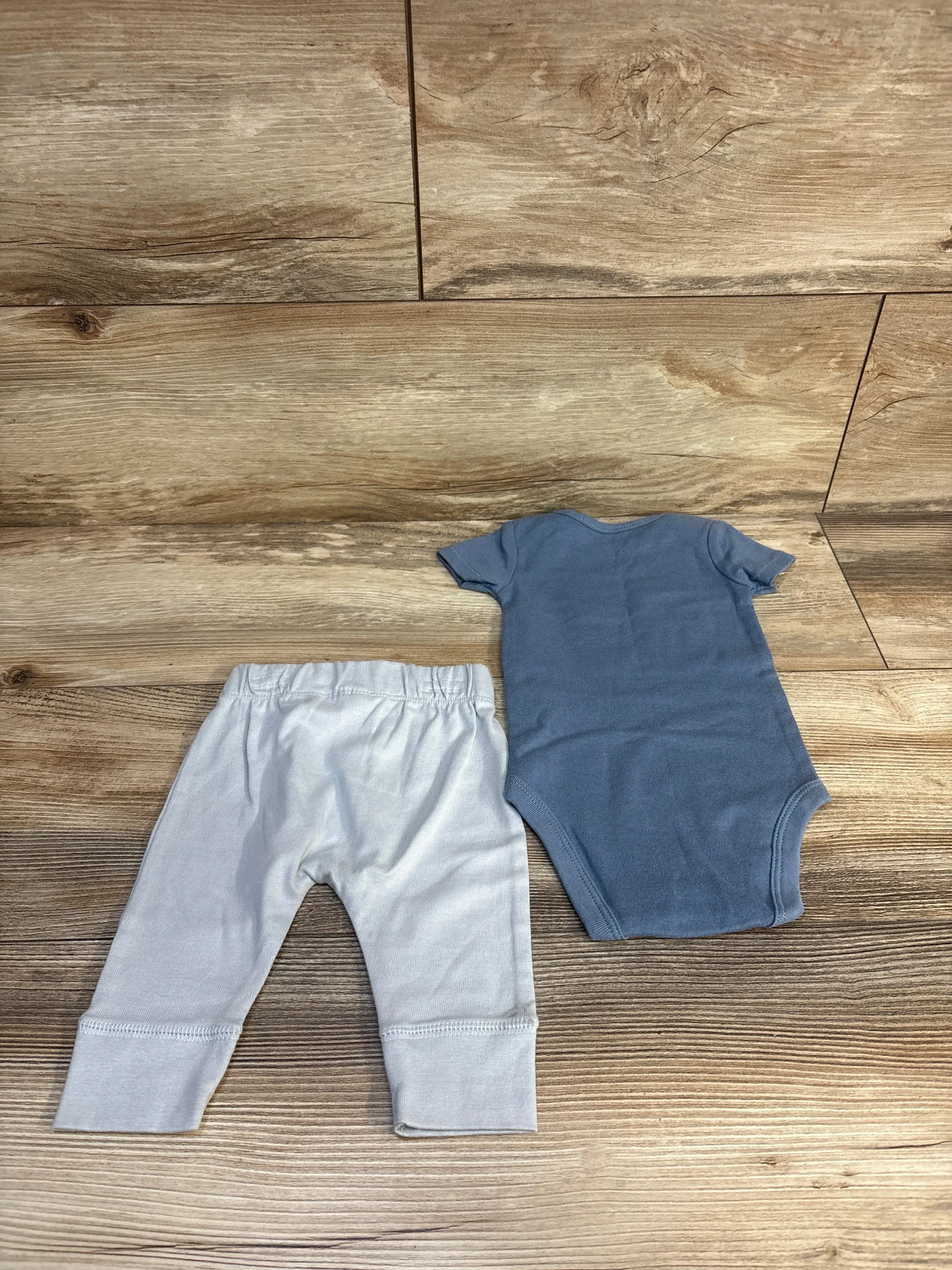 Blue baby onesie and light gray pants set on wood floor, kids clothing resale