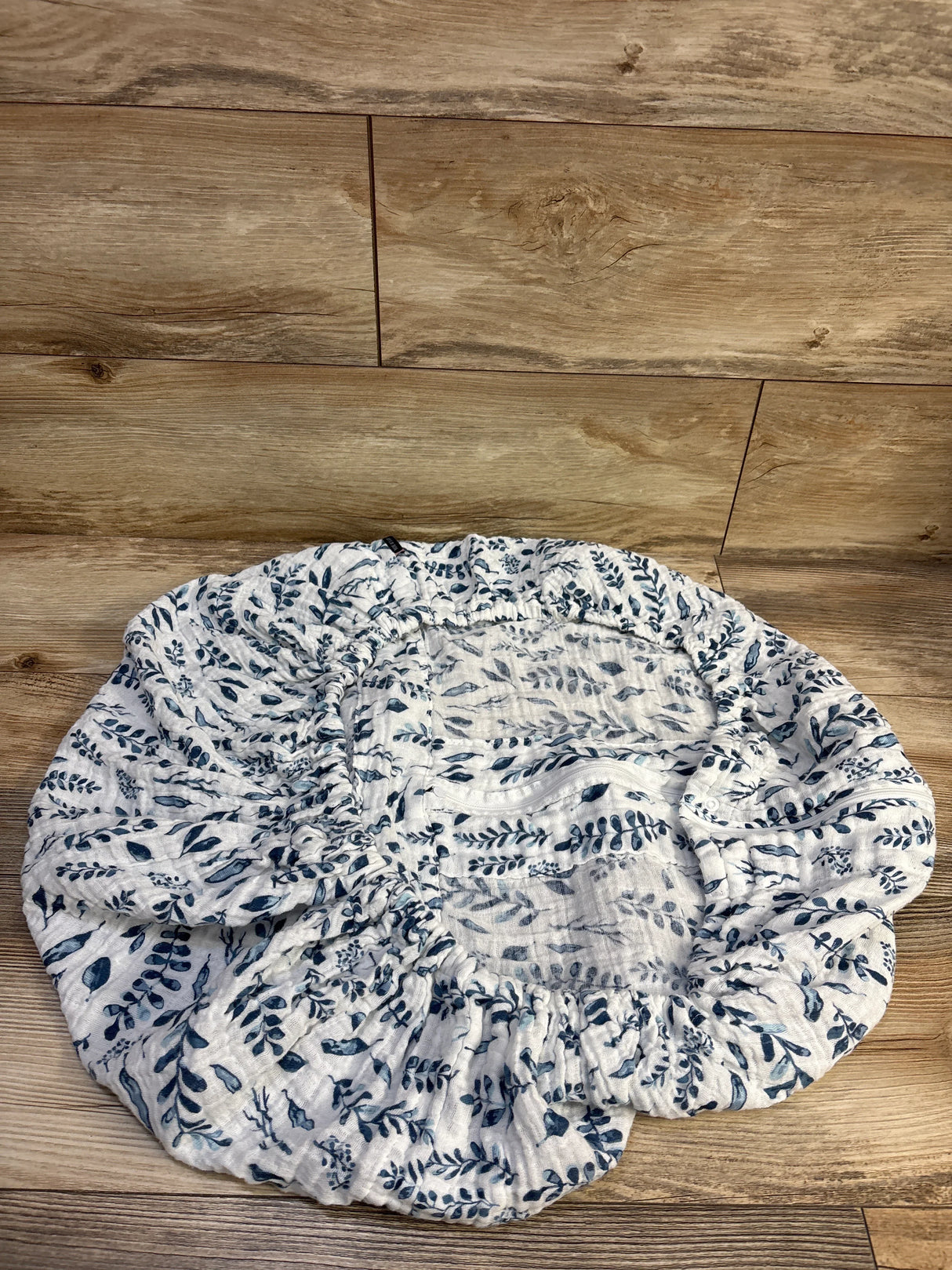 Top down view of Bebe au Lait muslin car seat cover showing navy leaf print and elastic edge on wood floor background