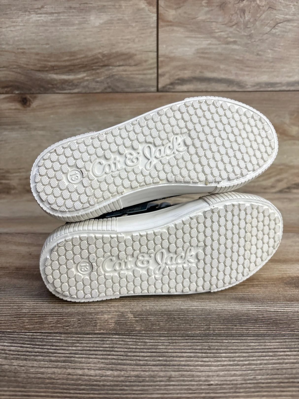 Bottom view of Cat and Jack Cora high-top sneaker showing white textured sole embossed with Cat and Jack logo on wood floor