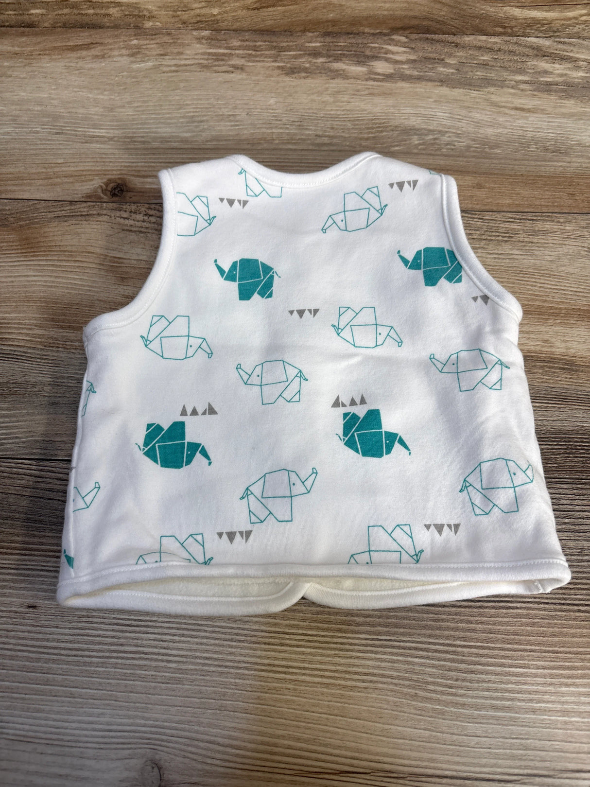 White baby vest with teal origami elephant print, laid flat on wood background