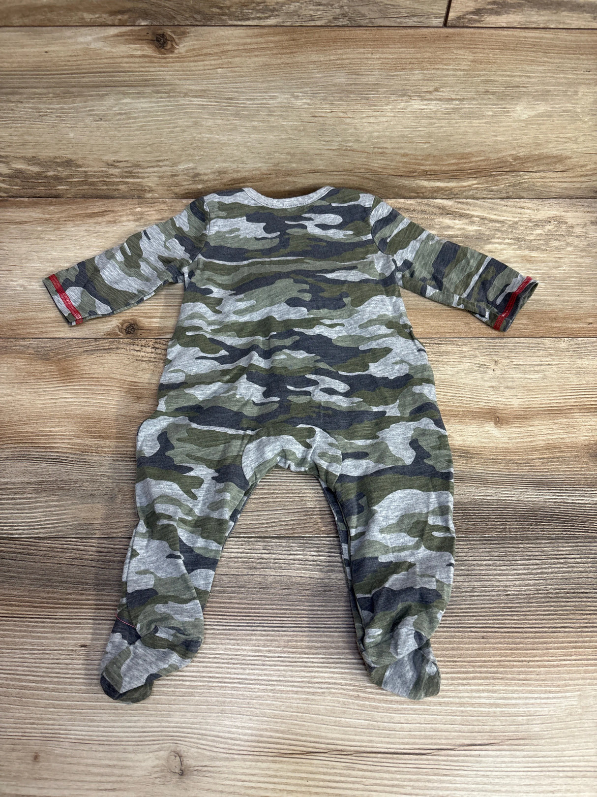 Baby romper with green and gray camouflage print and red trim on wooden background