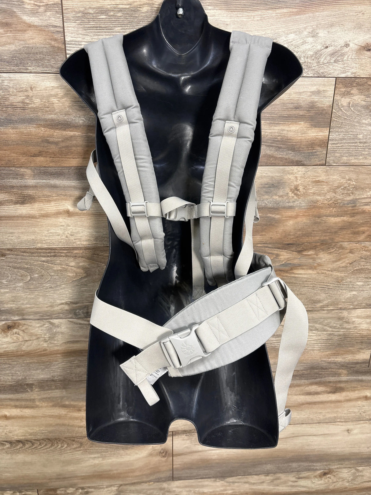 Light gray baby carrier with padded straps and buckles displayed on black mannequin torso