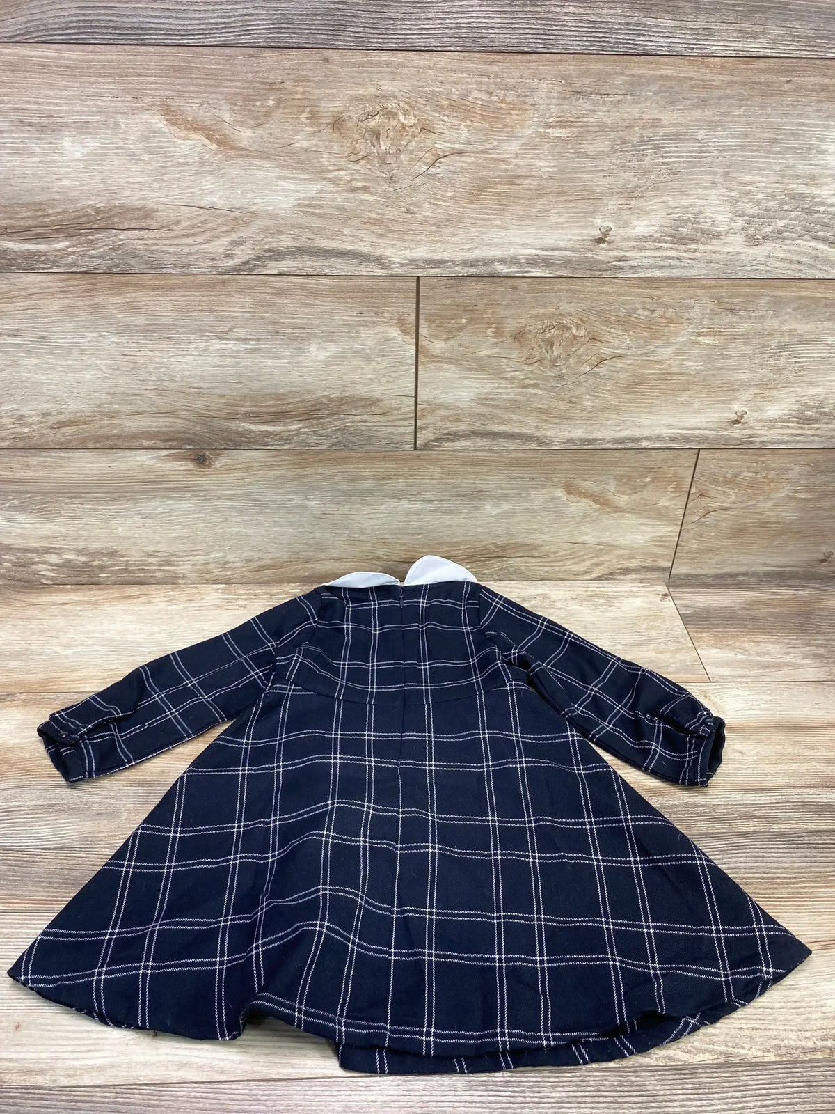 Flat lay of navy plaid toddler dress with white Peter Pan collar, long sleeves, size 2T on wood background