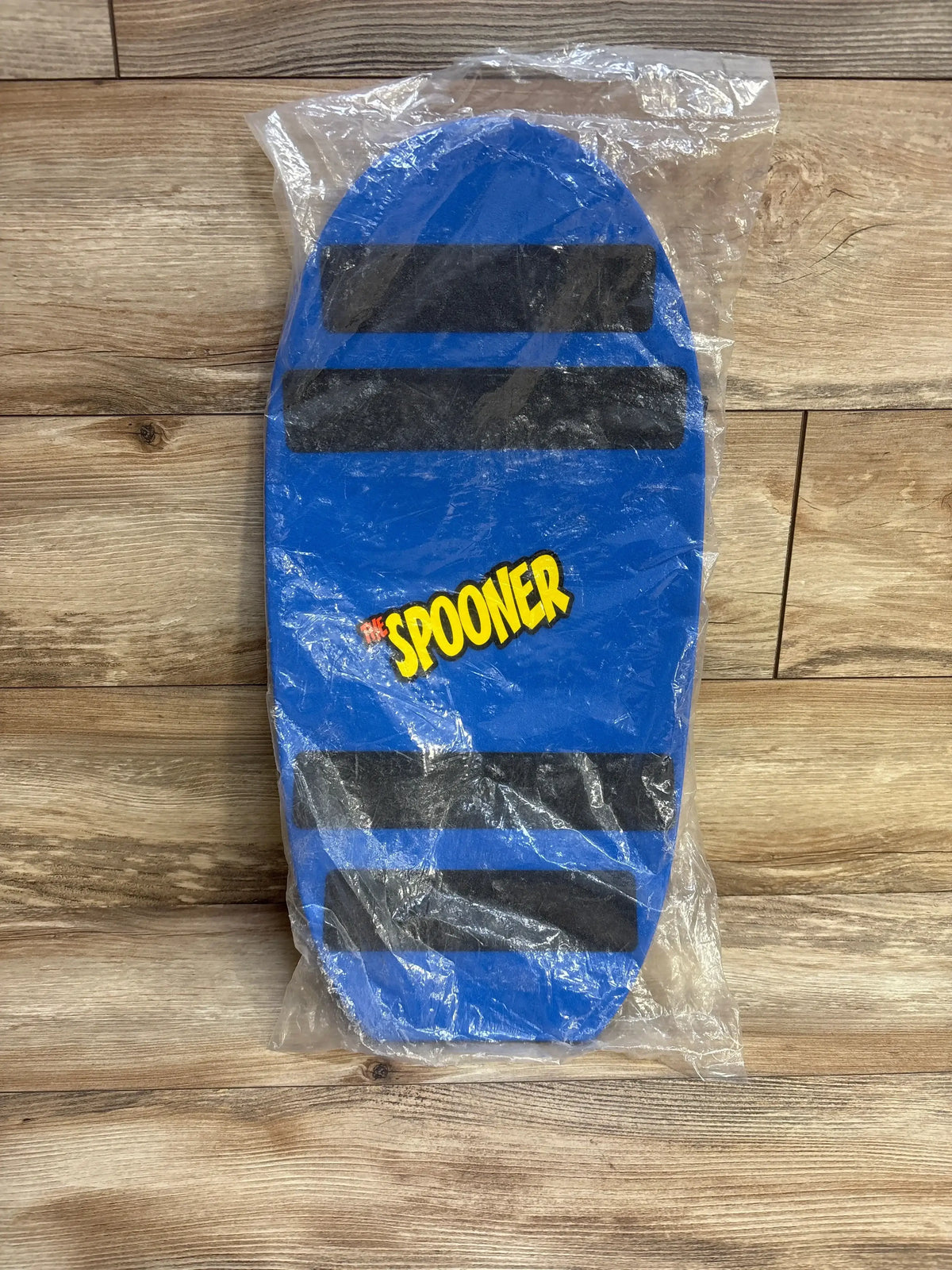 Top-down view of blue Spooner Board Pro with three black traction strips and SPOONER logo in clear plastic wrap on wooden floor