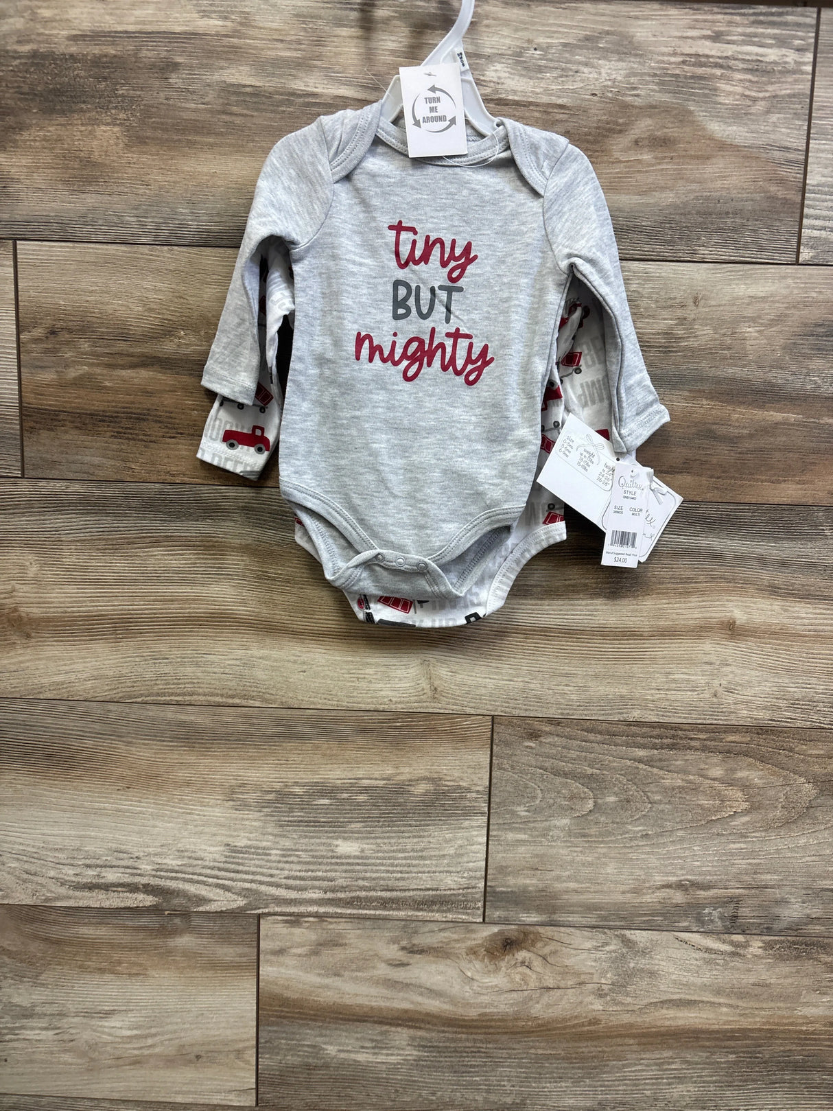 Front view of Quiltex grey long-sleeve baby bodysuit reading tiny but mighty with red truck print bodysuit behind, size 3-6m