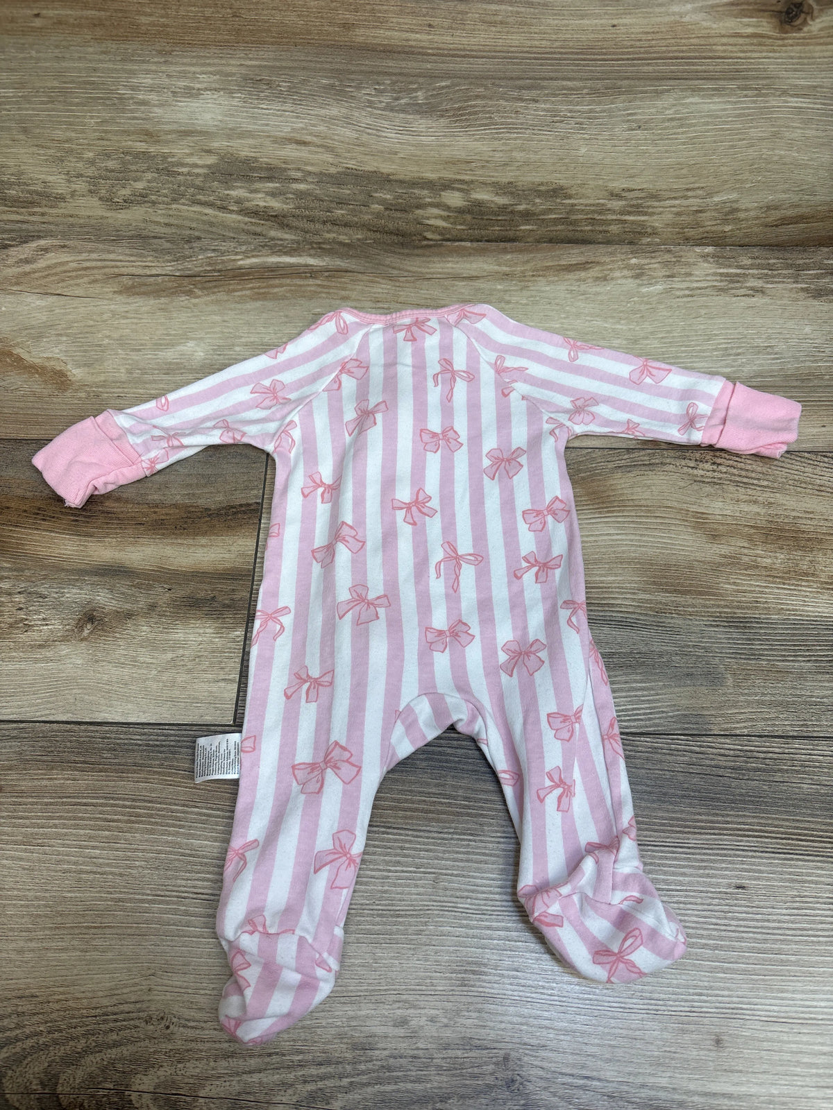 Top-down view of a pink and white striped Yoofoss footed sleeper with bow patterns on a wood surface