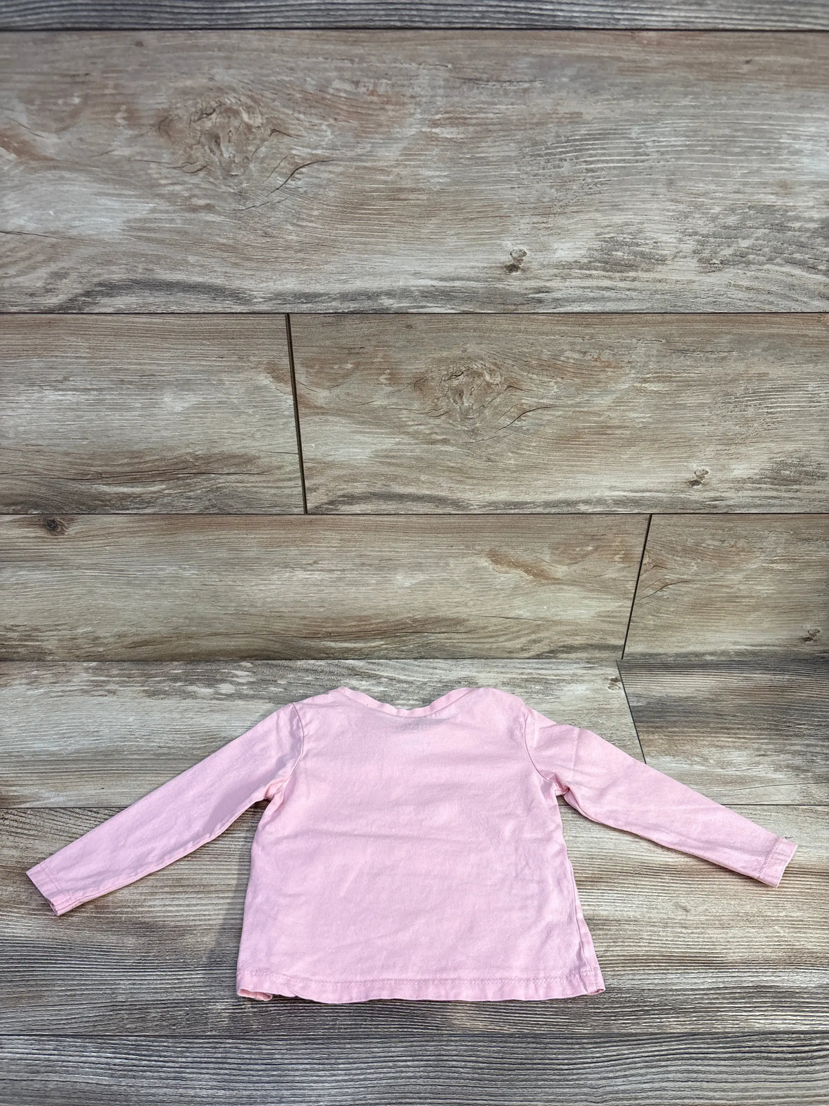 Back view of a pink Honest Baby long sleeve solid shirt for baby size 12m on a wood background