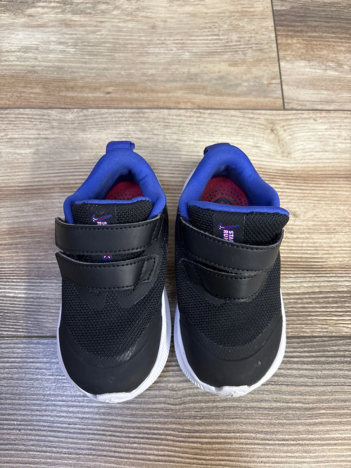 Rear view of Nike Star Runner TD Black Pink Rise sneakers showcasing hook-and-loop straps and blue lining on a wood-look floor
