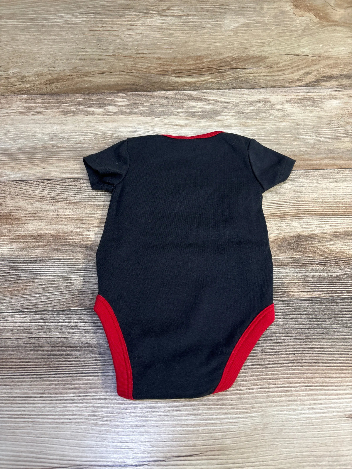 Back view of a black baby bodysuit with red trim on a wooden background.