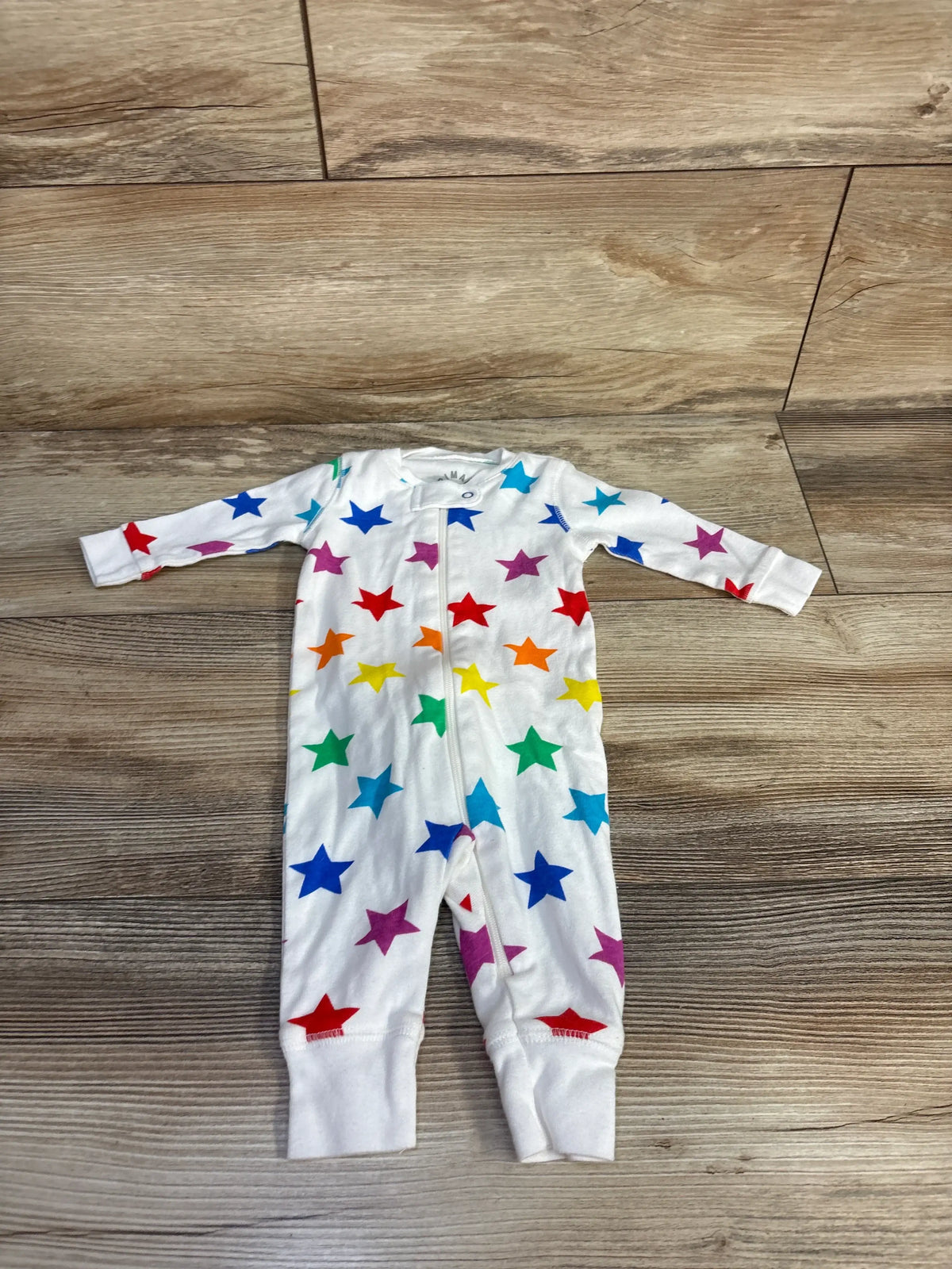 Front view of a white organic cotton star-print sleeper showcasing long sleeves, footed legs, and front zipper with a wood-look floor background