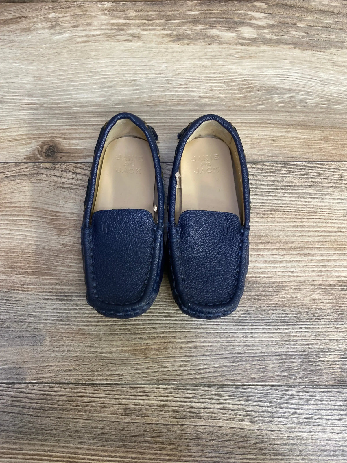 Top view of Janie & Jack navy leather driving shoes, size 8C, showcasing pebbled leather and moccasin stitching on wood