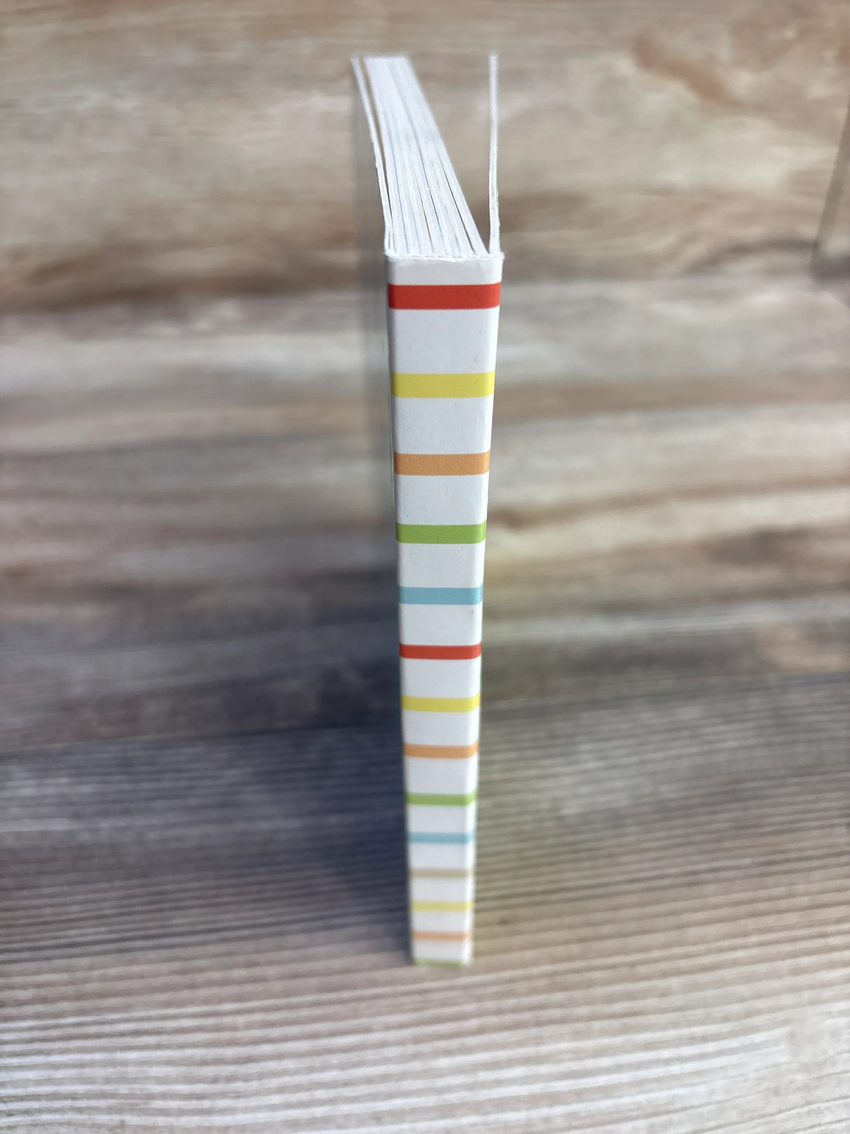 Colorful striped notebook spine on wooden surface, vertical view