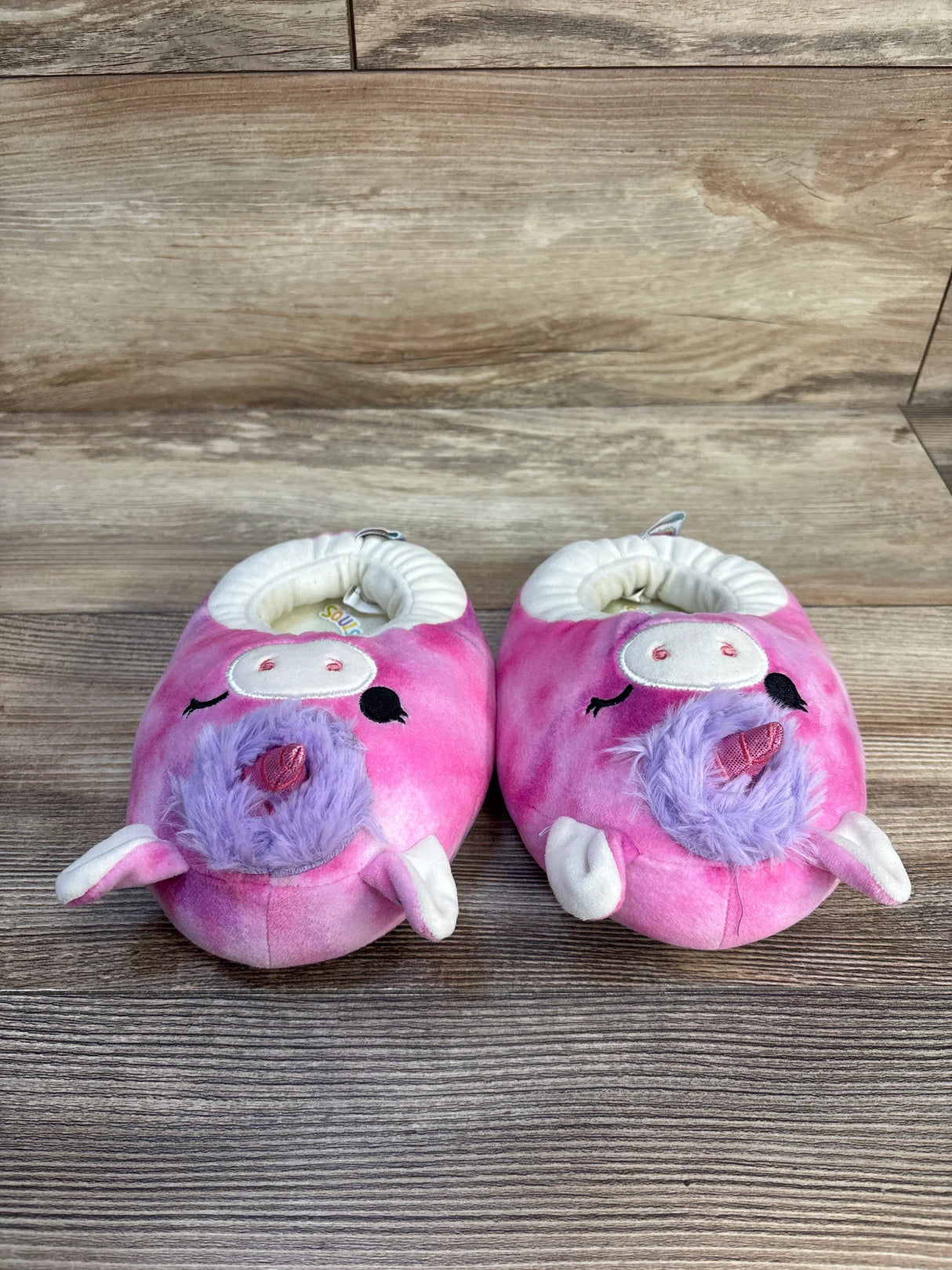 Pink plush unicorn baby slippers with purple mane on wood floor