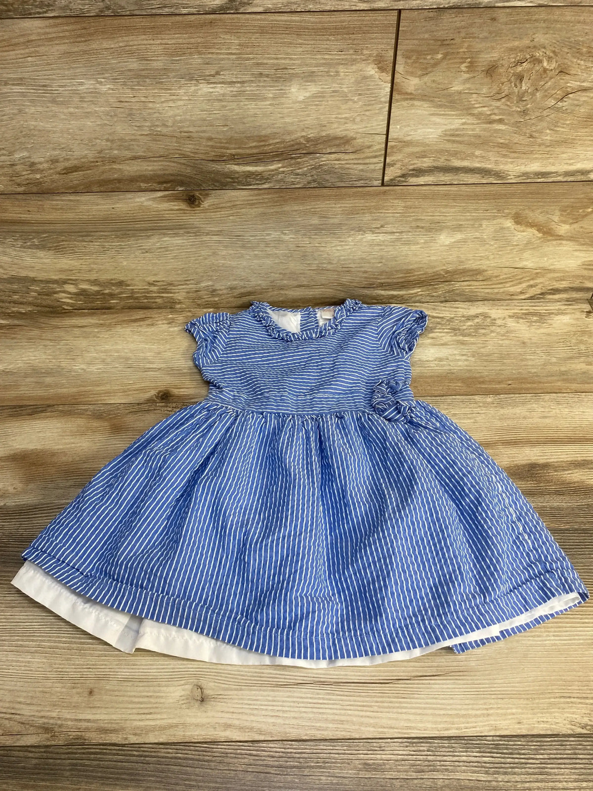 Flat lay of blue striped seersucker toddler dress (3T) with ruffled cap sleeves, gathered skirt and lining on wood floor