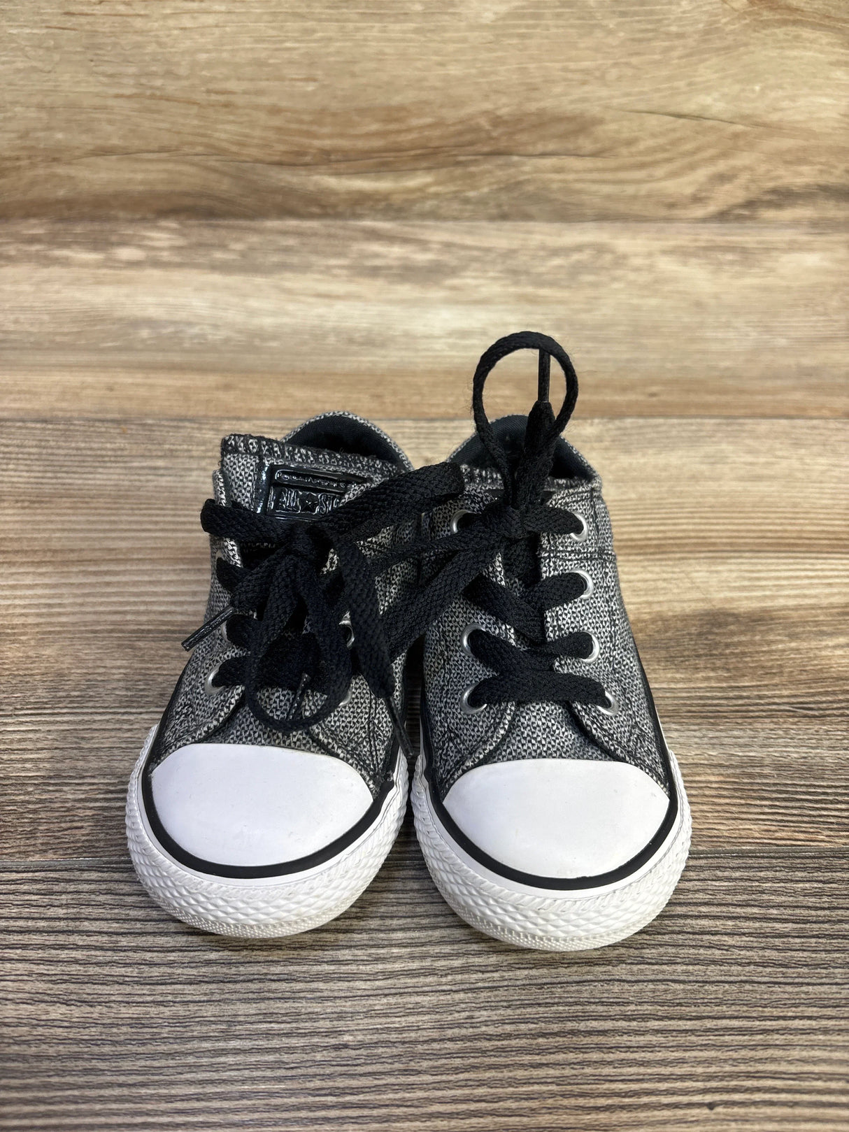 Front view of Converse Madison Ox toddler low-top sneakers in grey with white rubber toe caps and black laces on wood background