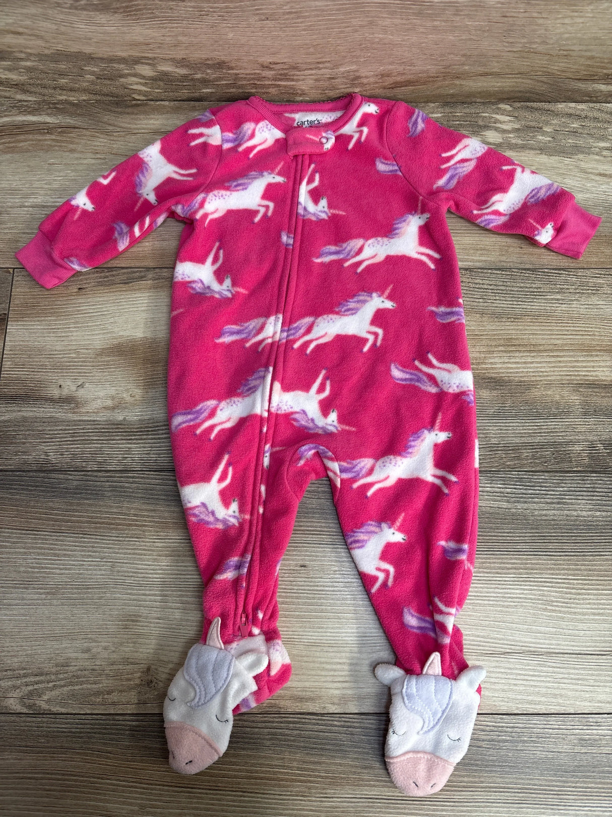 Pink baby onesie with unicorn pattern and unicorn face slippers on wooden floor